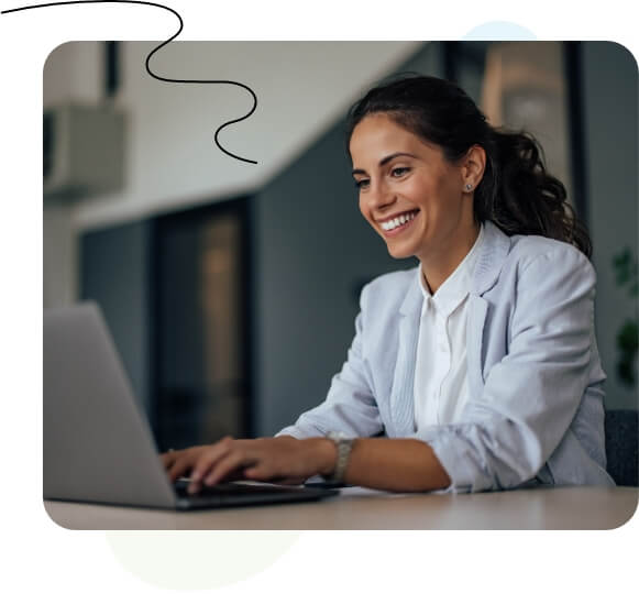 A woman sitting at a desk, typing on a laptop in front of a whiteboard.