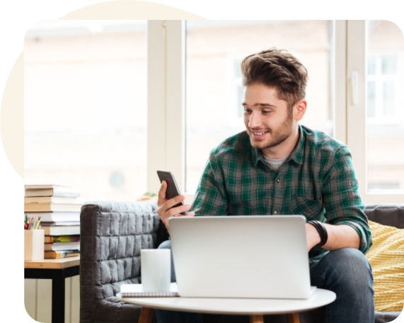 Hombre delante de una computadora portátil y revisando el teléfono