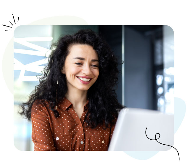 A woman smiling at a laptop screen, looking happy and engaged.