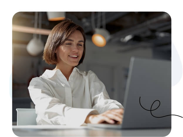 A woman focused on her laptop screen in a modern office setting.
