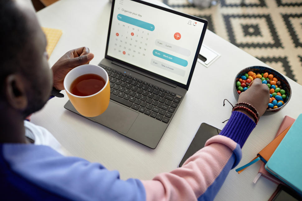 High angle portrait of black man enjoying candy snack and coffee while using laptop at desk, copy space