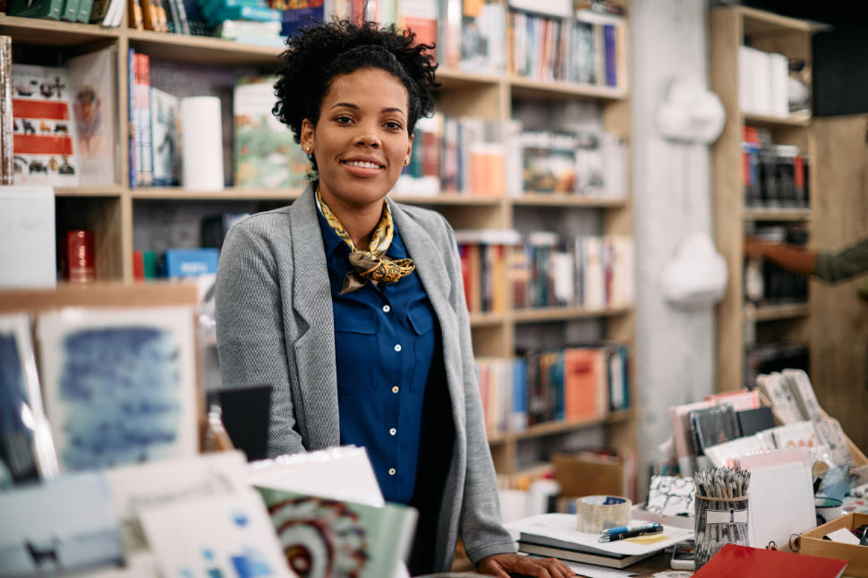 Happy African American saleswoman at bookstore checkout looking at camera.