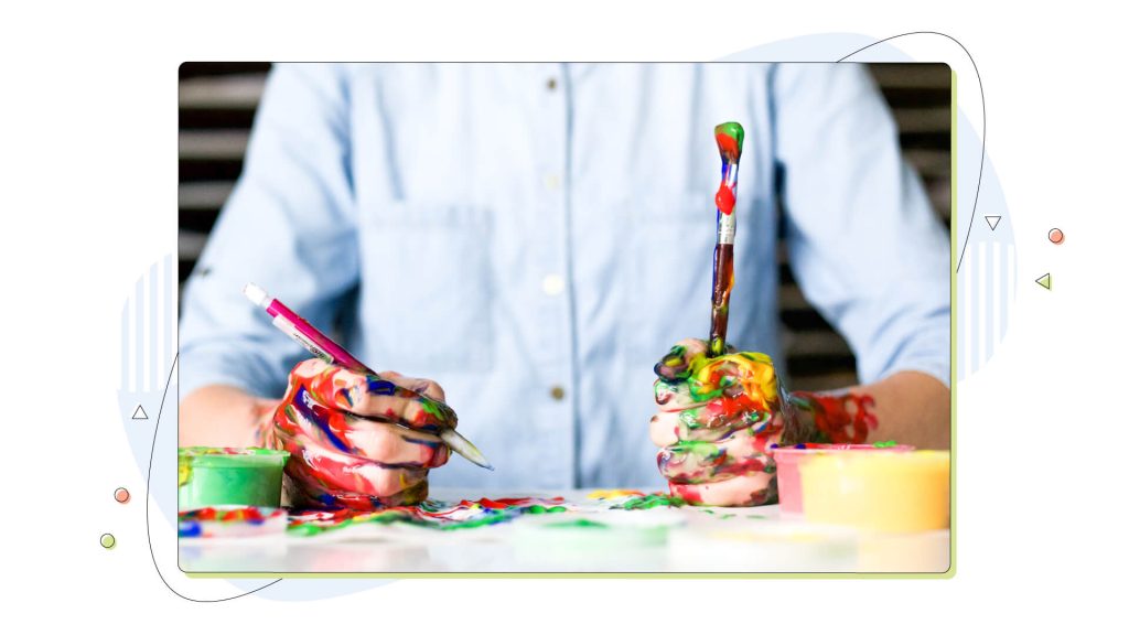 Person with painted hands holds a brush and a pen