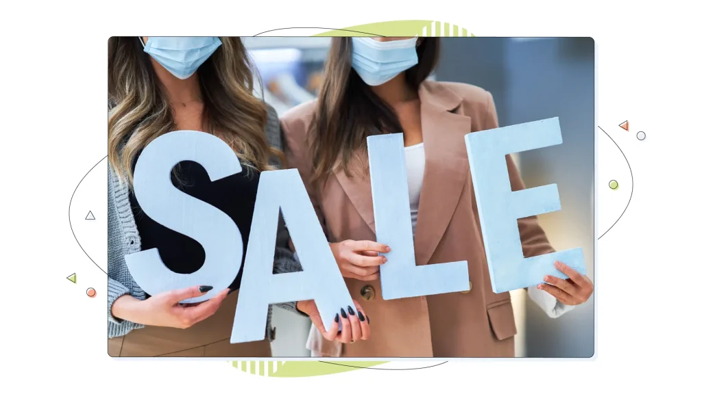 Two women shopping holding a SALE sign.