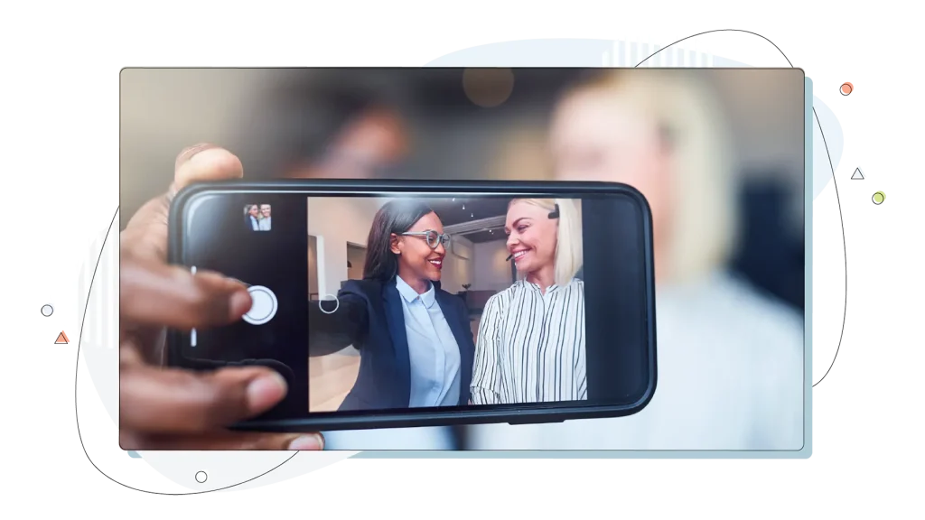 Two smiling young businesswoman using a cellphone to take selfies.
