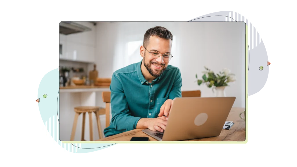 Man smiling while working on his laptop wearing a blue shirt.