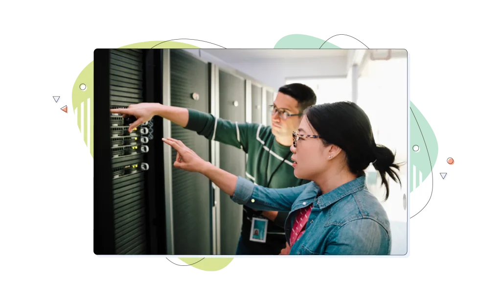 Two people in a server room, pointing toward a server rack system.