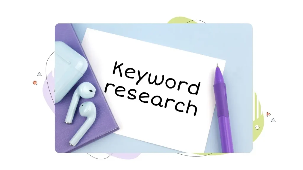 Keyword research is written on a piece of paper next to a pen and headphones on a desk.