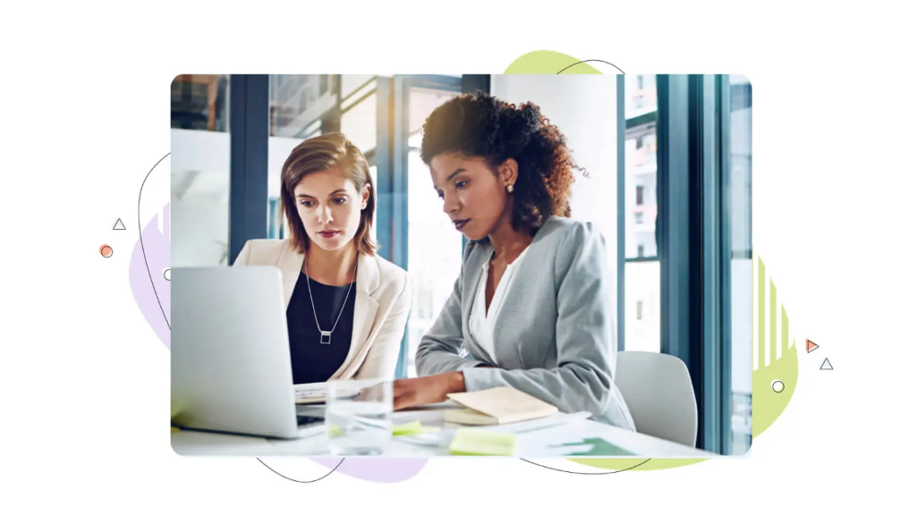 Two colleagues sit together reviewing business results on a laptop to learn how to check domain worth.