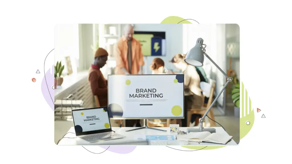 A marketing team meets around a table. A desktop computer in their office displays the words ‘Brand Marketing’ on its screen as they discuss premium vs. regular domain strategies.