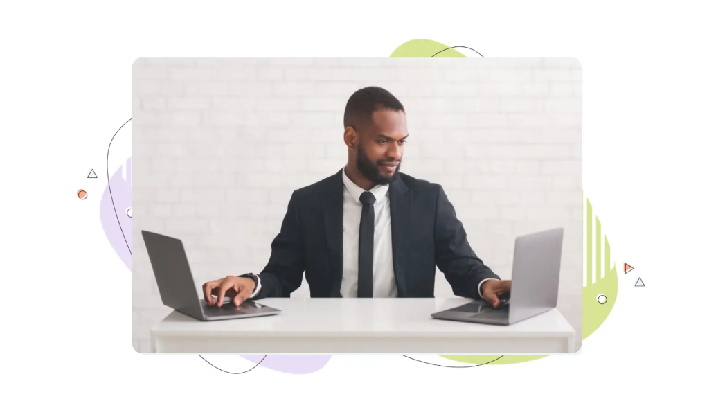 Businessman working simultaneously on two laptops at a white desk, illustrating a comparison of VPS vs shared hosting.